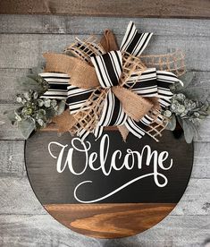 a welcome sign hanging on the side of a wooden wall with burlocks and greenery