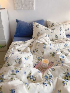 an unmade bed with blue flowers on it and a candle in the middle,