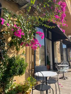 tables and chairs are outside in front of a building with pink flowers on the windows