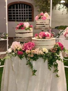 three tiered wedding cake with pink and white flowers on the top, surrounded by greenery