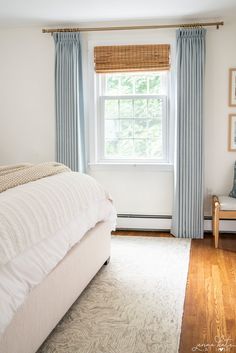 a white bed sitting under a window next to a wooden floor covered in blue curtains