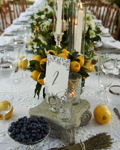 the table is set with lemons, blueberries, and candles for an elegant dinner