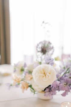 a white vase filled with flowers on top of a table next to a lit candle