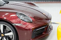 the front end of a red sports car parked in a garage with two yellow cars behind it