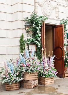 two wooden planters filled with flowers next to a door and window sill on the side of a building