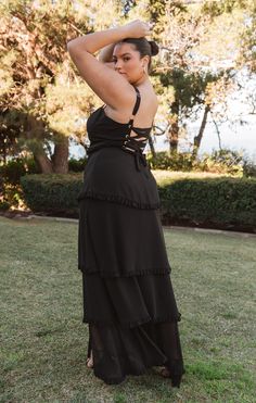 a woman in a black dress is standing on the grass with her hands behind her head