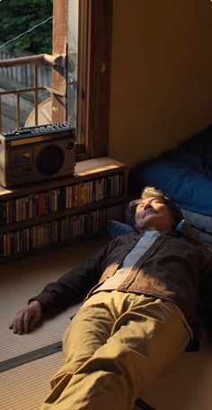 a man laying on the floor in front of a window next to a book shelf