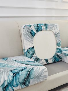 a white couch with blue and green palm leaves on it, next to a window