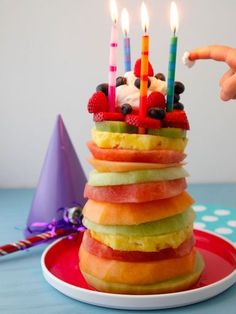 a birthday cake made out of fruit and candles is on a plate with a party hat in the background