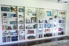 a living room filled with lots of books on top of a white book shelf next to a rug