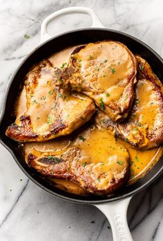 pork chops with gravy in a skillet on a marble countertop