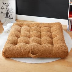 a brown dog bed sitting on top of a wooden floor next to a blackboard