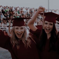 two women in graduation caps and gowns posing for the camera with their arms up