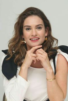 a woman posing for a photo with her hands on her chin and wearing gold earrings