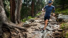 a man running down a rocky trail in the woods with lots of trees around him