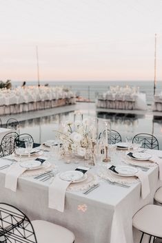 the table is set with plates and silverware for an elegant dinner by the water