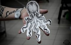 an octopus sticker is held in someone's hand with tattoos on their arm