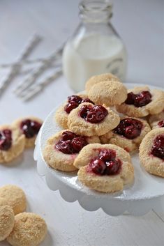 small cookies with jam are on a plate next to a bottle of milk and spoons