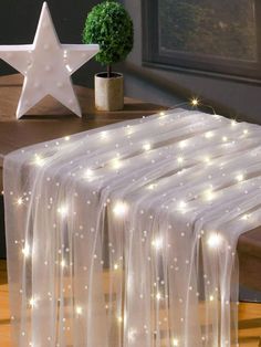 a white table cloth with lights on it and a star decoration above the table behind it