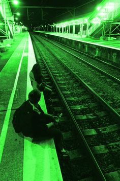 a woman sitting on the ground next to train tracks in a green lit subway station