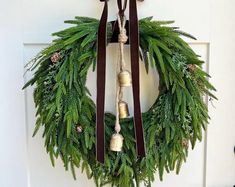 a wreath with bells hanging from it on the front door, decorated with evergreen leaves and pine cones