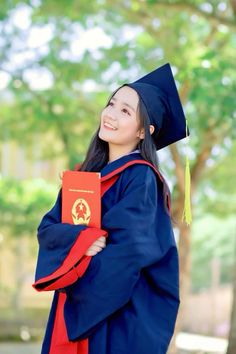 a woman in blue graduation gown and cap holding a red book smiling at the camera