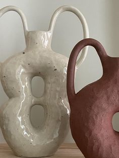 two white and brown vases sitting next to each other on a wooden table in front of a wall