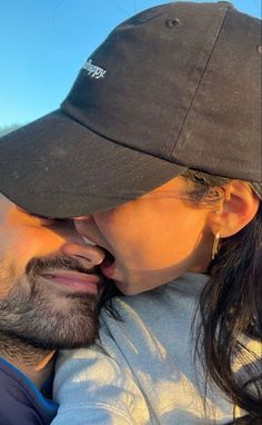 a man and woman kissing each other while they are wearing baseball caps on their heads