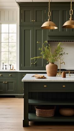 a kitchen with green painted cabinets and gold pendant lights over the island, along with a potted plant