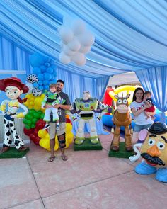 some people are standing in front of balloons and cartoon character statues at a party with blue drapes on the ceiling