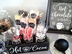 an assortment of hot chocolates and candies in glass jars on a table next to a chalkboard sign