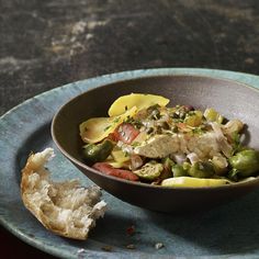 a bowl filled with fish and vegetables on top of a blue plate next to a piece of bread