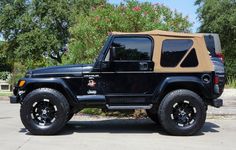 a black jeep parked in a parking lot next to some trees and bushes on a sunny day