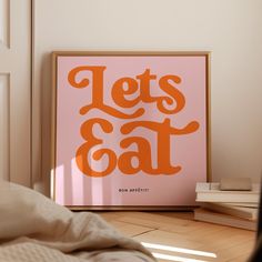 an orange poster that says let's eat on it in front of a bed