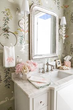 a bathroom sink with a mirror above it and flowers on the counter next to it