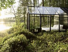 a small glass house in the middle of some grass and trees with sun shining on it