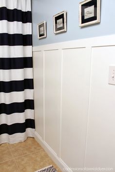 a bathroom with black and white striped shower curtain next to the bathtub in front of two framed pictures on the wall