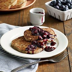 two pancakes with blueberries and syrup on a white plate next to a cup of coffee