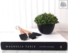 there is a black book with the words magnolia table written on it next to a potted plant