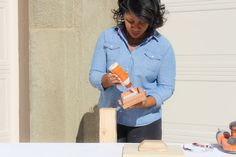 a woman standing next to a wooden block with an orange object in it's hand