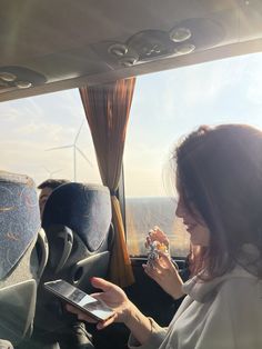 a woman sitting in the back seat of a car holding a cell phone and looking at her tablet