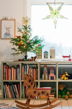 a wooden rocking horse sitting in front of a book shelf filled with books next to a christmas tree