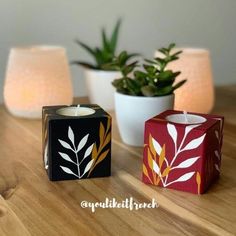 two candles sitting on top of a wooden table next to plants and a potted plant