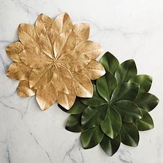 two gold leaves on top of a white marble table next to a green leafy plant