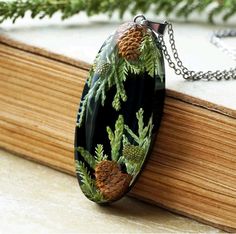 a glass pendant with pine cones on it sitting on top of a wooden box next to a tree branch