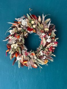 a wreath with dried flowers and leaves on a blue background is hanging on the wall