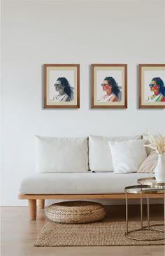 a living room with white couches and paintings on the wall above them, along with a wicker coffee table