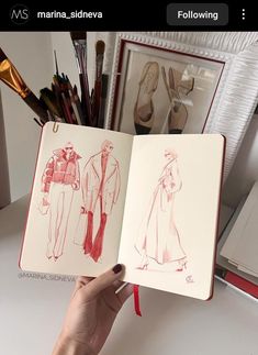 a hand holding an open book with drawings of people in dresses and coats on it