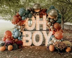 a sign that says oh boy surrounded by balloons and pumpkins in front of some trees