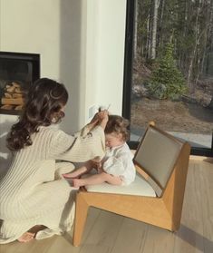 a woman combing a child's hair while sitting on a chair in front of a fireplace